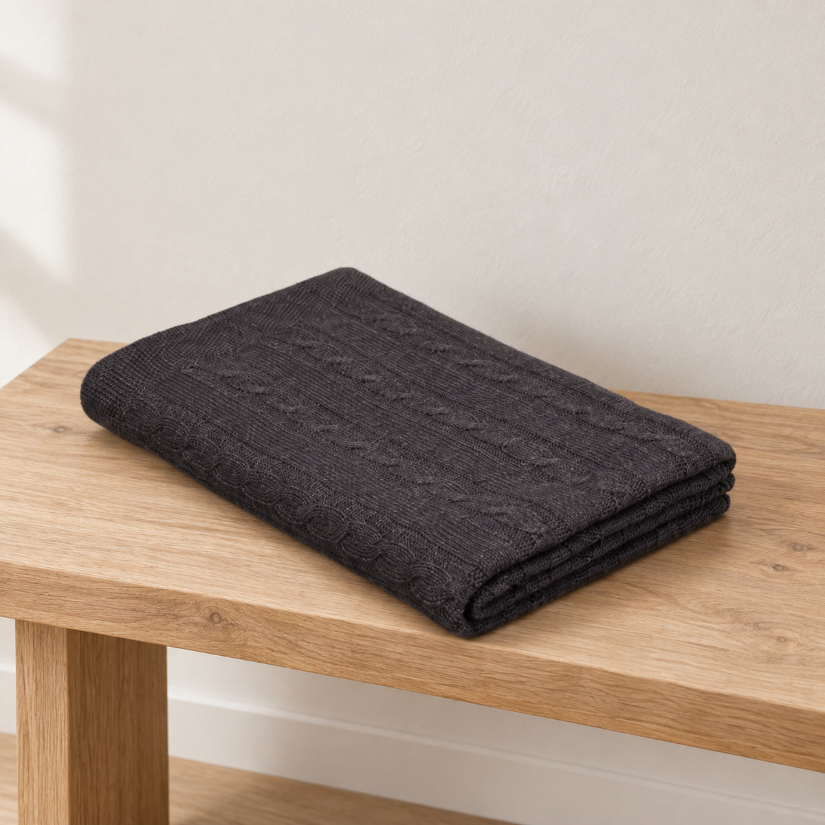 Pislak Pleta Wool-Blend Knitted Throw in anthracite, folded on a wooden bench, showing the cable-knit texture.