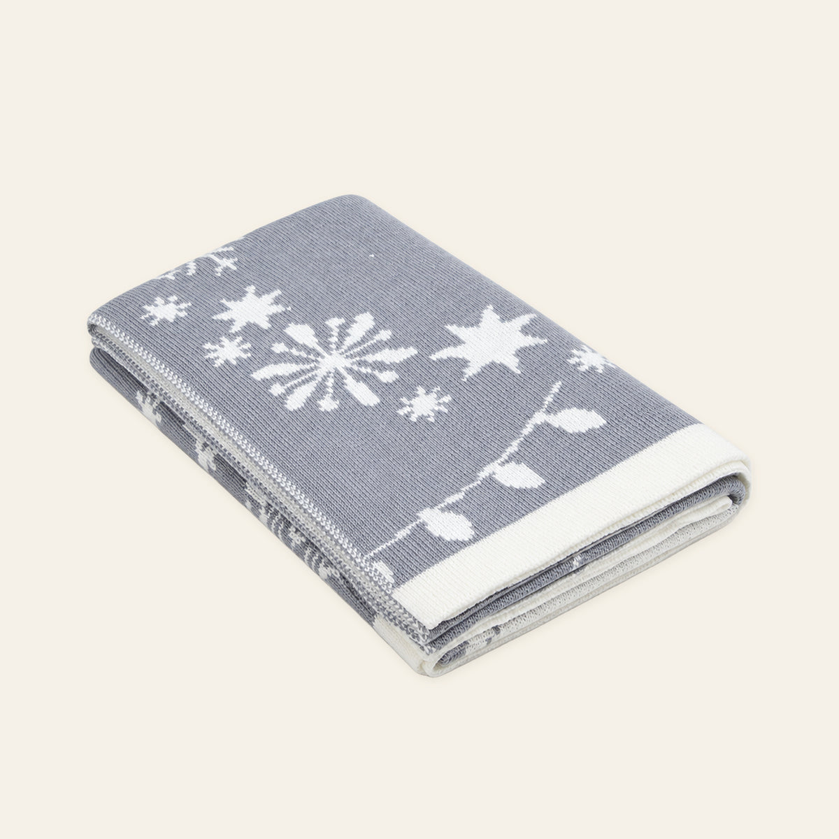 Pislak Sneg merino-blend throw in grey and cream, neatly folded in a studio view showing its snowflake motifs.