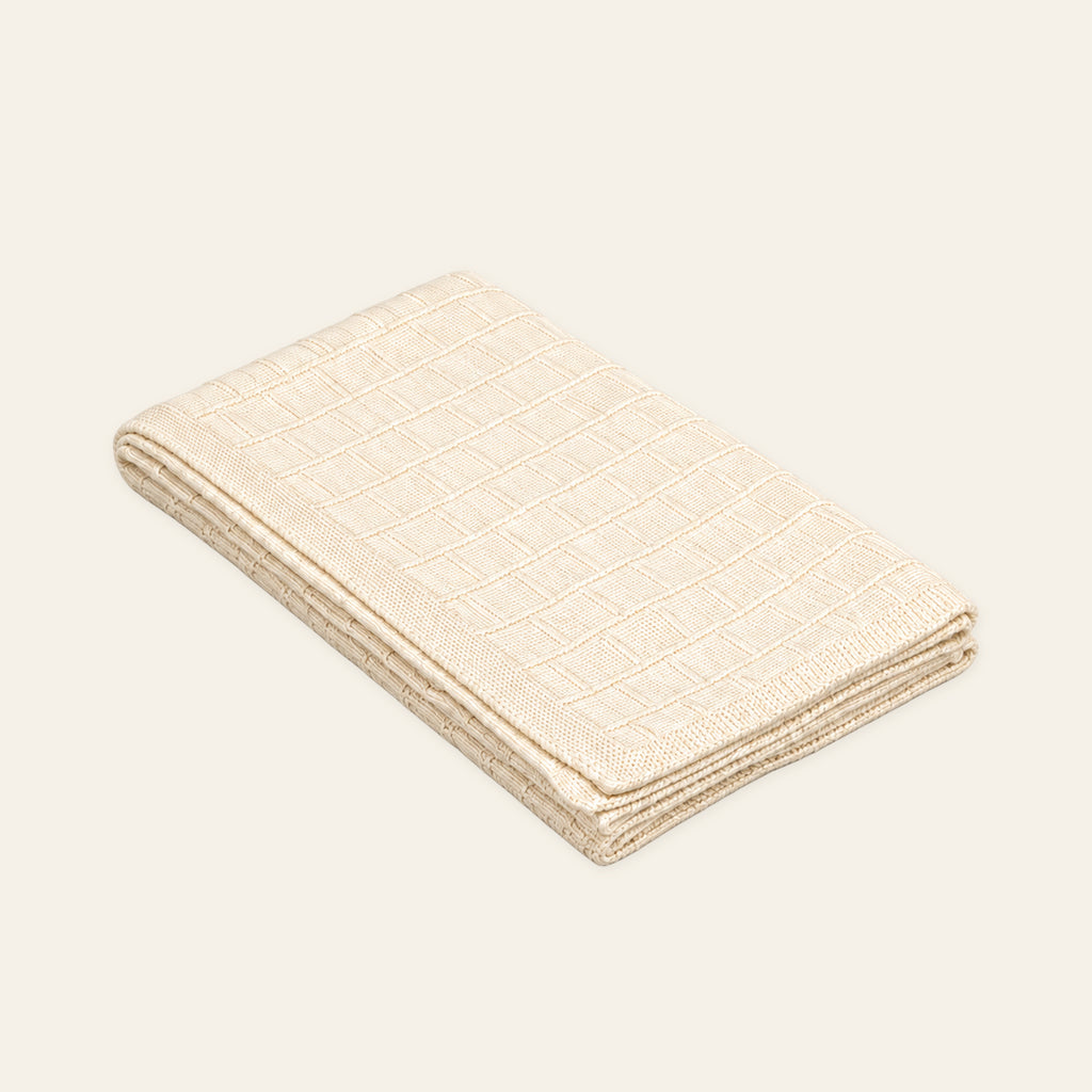 Pislak Buba Baby Knitted Blanket in cream, folded with a fine checked knit pattern and small black tab.