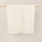 Pislak Buba Baby Knitted Blanket in cream, folded over a wooden rail, showing the fine checked knit.