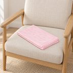 Alex baby blanket in light pink, folded on a seat with small oval motifs visible.