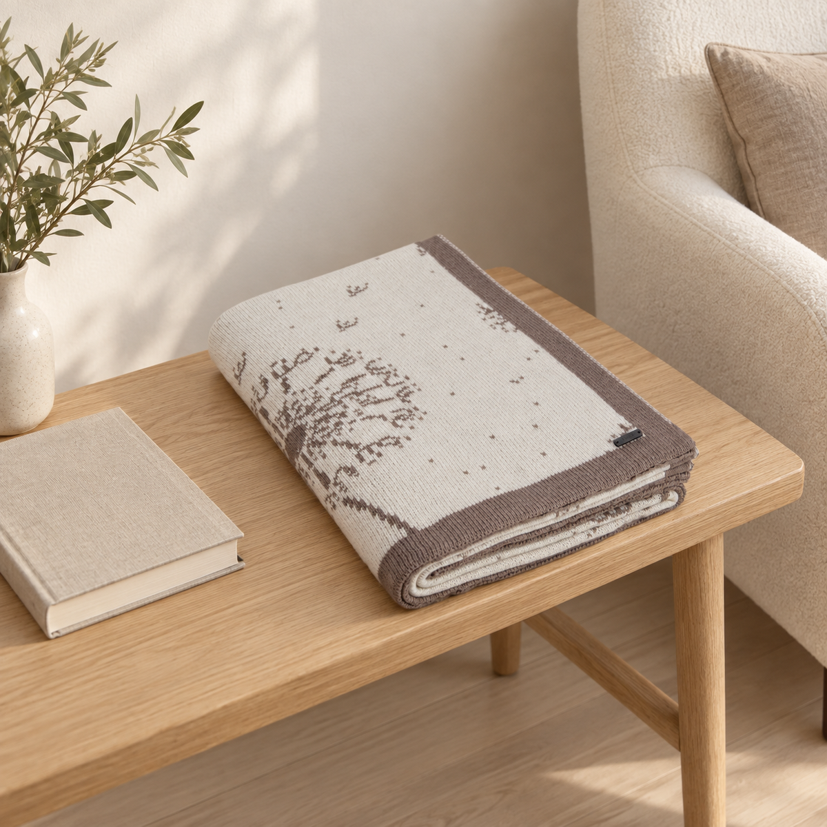 Dalia blanket in sand and cream, folded on a bench with its dandelion pattern visible.