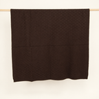 KARO throw in dark brown, hanging folded to show its diamond knit and lower border.