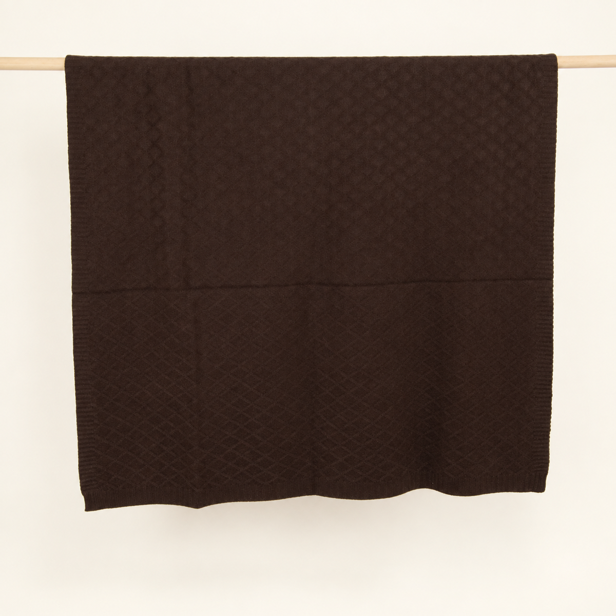 KARO throw in dark brown, hanging folded to show its diamond knit and lower border.