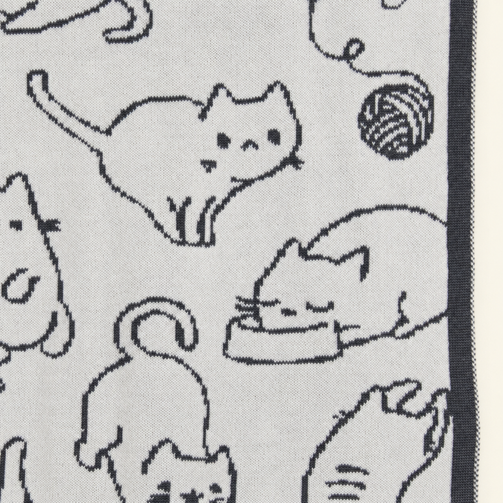 KITTY blanket in grey and cream, detail of cat motifs, a ball of yarn and the dark border.