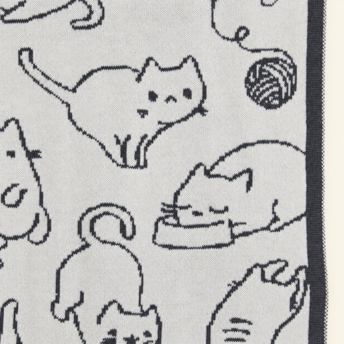 KITTY blanket in grey and cream, detail of cat motifs, a ball of yarn and the dark border.