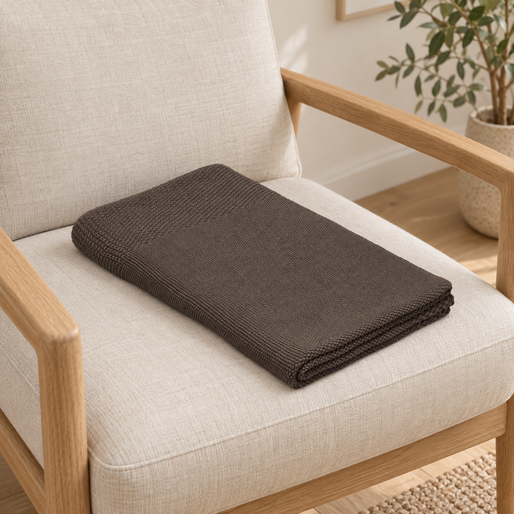 Tinka throw in taupe, folded on an armchair seat with its textured border visible.